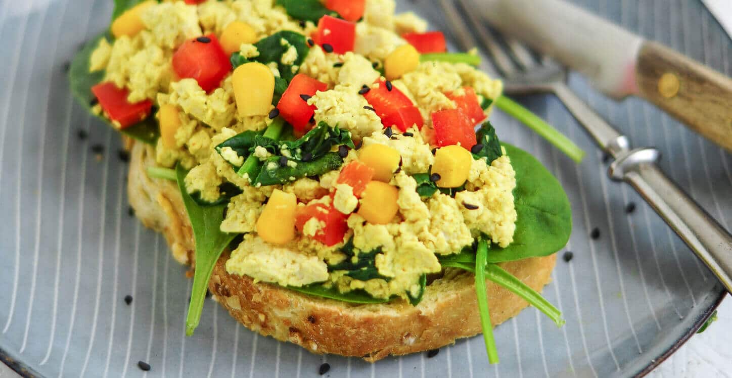 Veganes Rührei aus Tofu mit Kurkuma, Paprika, Mais und Spinat auf einer Scheibe Brot