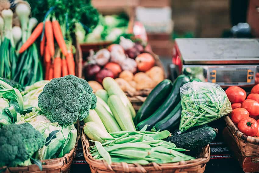 Frisches, veganes Gem&uuml;se wie Brokkoli, Zucchini, Tomaten und Karotten auf einem Marktstand.