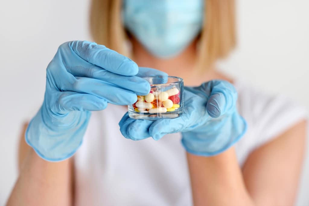 Woman's hands in gloves holds a glass with pills to be taken to her patient. Healthcare and medical concept.