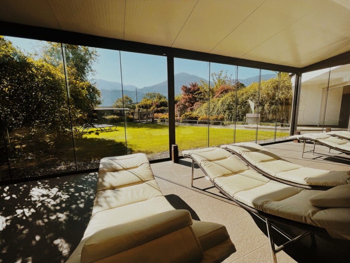 Entspannungsbereich mit Liegen und gro&szlig;em Fenster mit Blick auf Garten und Berge.