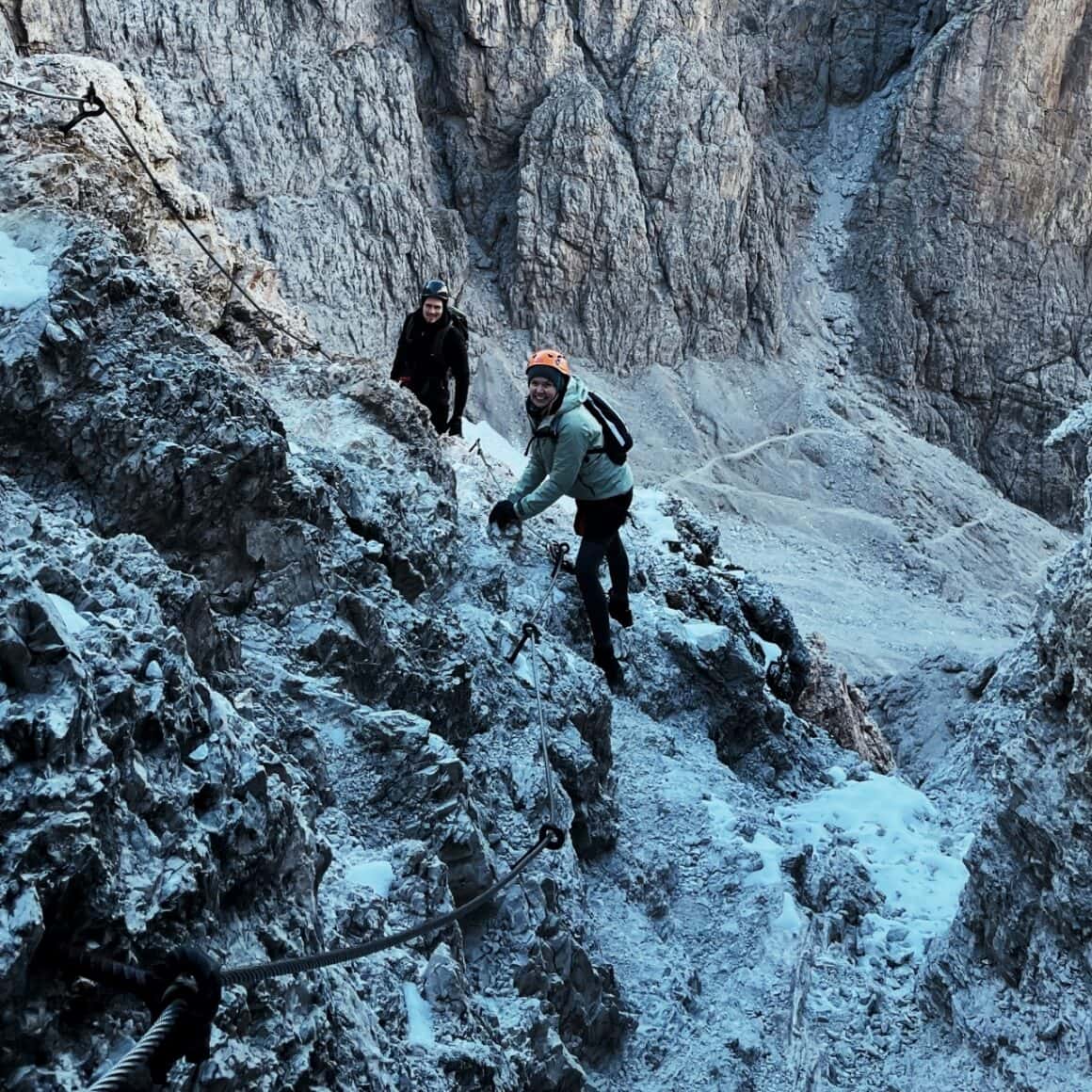 Zwei Bergsteiger erklimmen verschneiten Felsen im Gebirge.