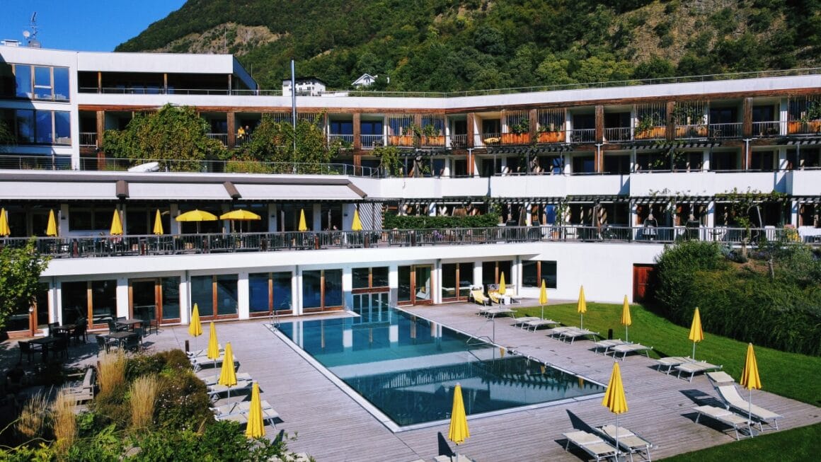 Modernes Hotel mit Pool, Sonnenschirmen und Liegen im Au&szlig;enbereich.
