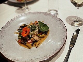 Veganer Gourmet-Teller mit Pasta, Gem&uuml;se und essbaren Bl&uuml;ten, serviert in einem eleganten Restaurant.