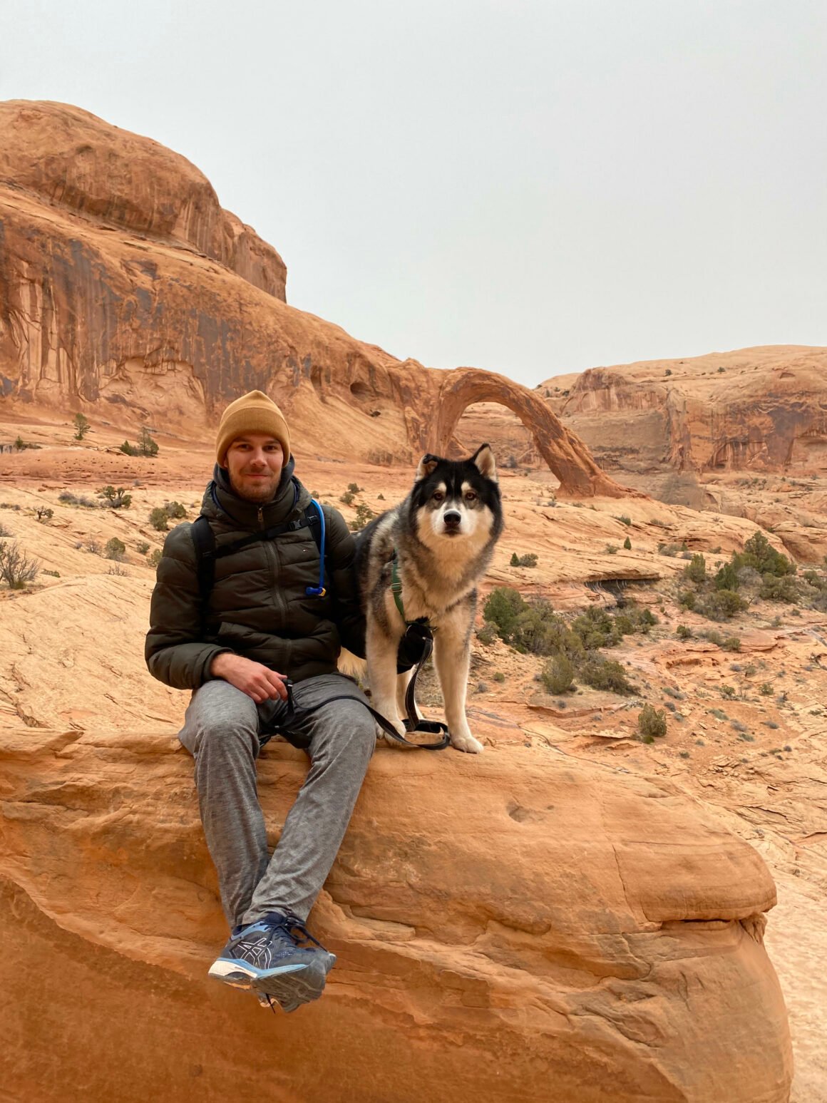 Mann sitzt in einer Landschaft aus Steinen mit einem Hund neben sich