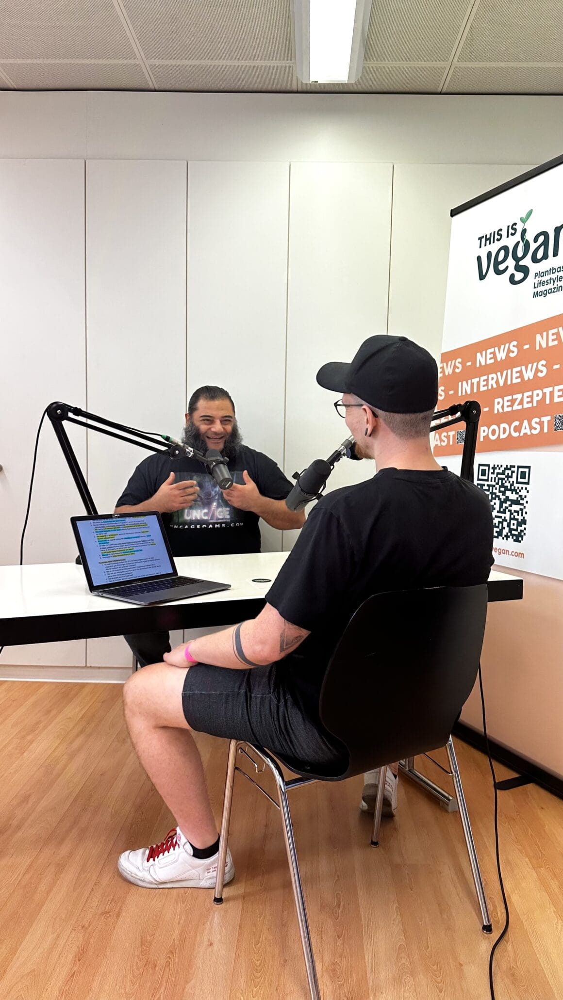 Yannick und Patrik Baboumian sitzen sich an einem Tisch gegenüber, auf dem Tisch steht und Laptop und jeder der Männer hat ein Mikrofon vor sich aufgebaut