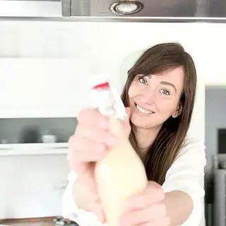 Ana hebt selbstgemachten veganen Eierlikör in einer Glasflasche hoch