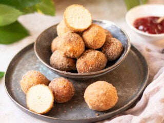 Vegane Quarkbällchen auf einem Teller, mit Zimt-Zucker bestäubt, goldbraun und frisch frittiert