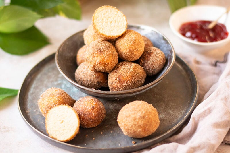 Vegane Quarkbällchen auf einem Teller, mit Zimt-Zucker bestäubt, goldbraun und frisch frittiert