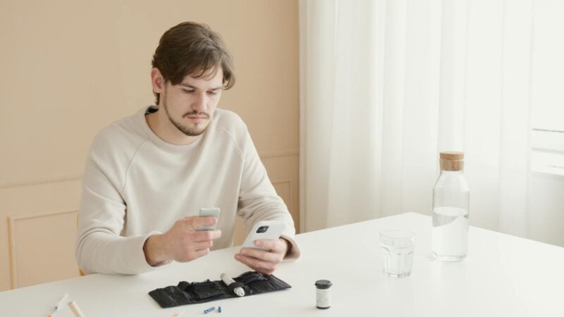 Mann testet Gesundheitswerte mit Selbsttest-Kit und Smartphone am Tisch