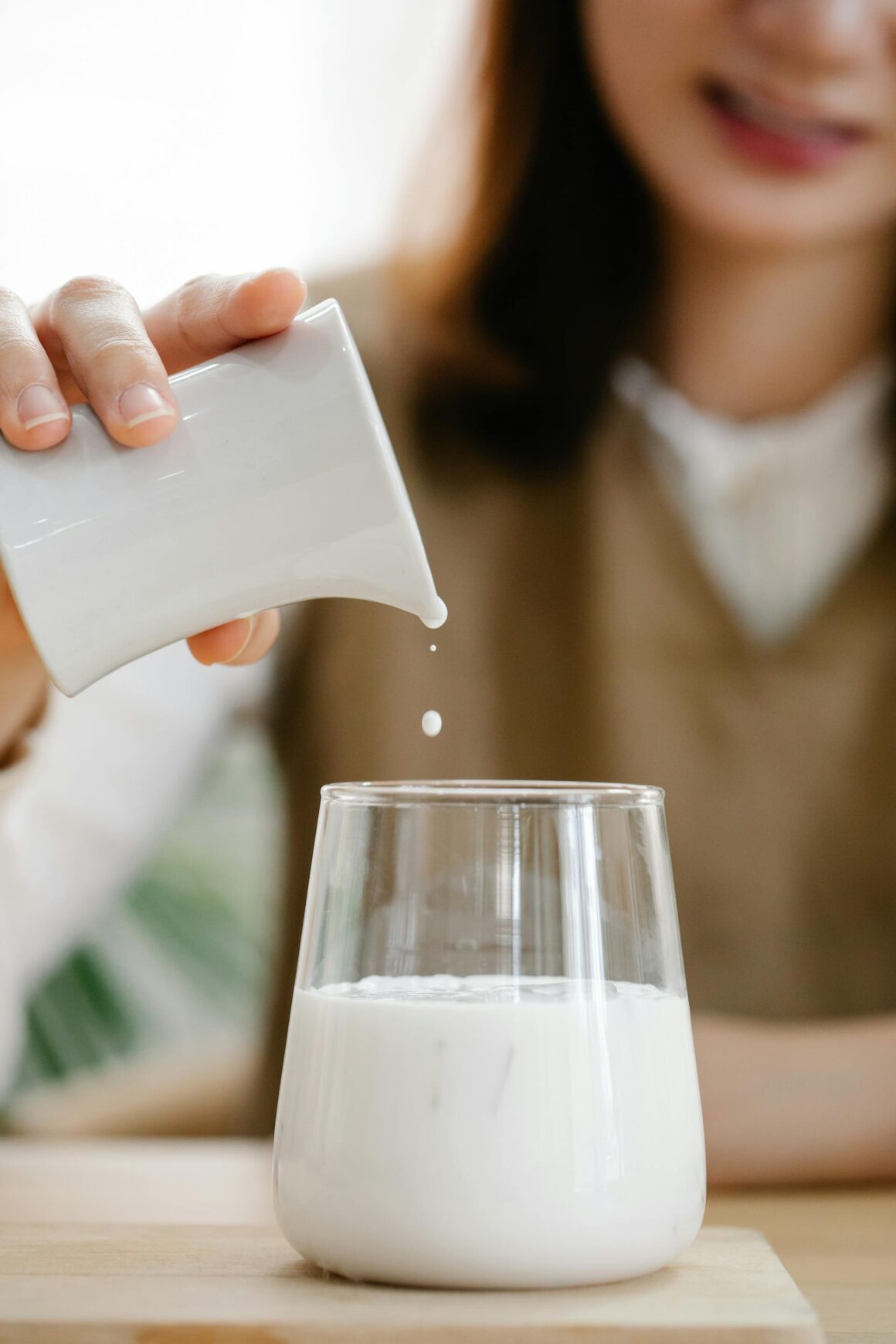 Frau gießt pflanzliche Milch in ein Glas