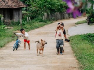 Ein Gruppe kleiner Kinder läuft mit ihrem Hund durch das Dorf