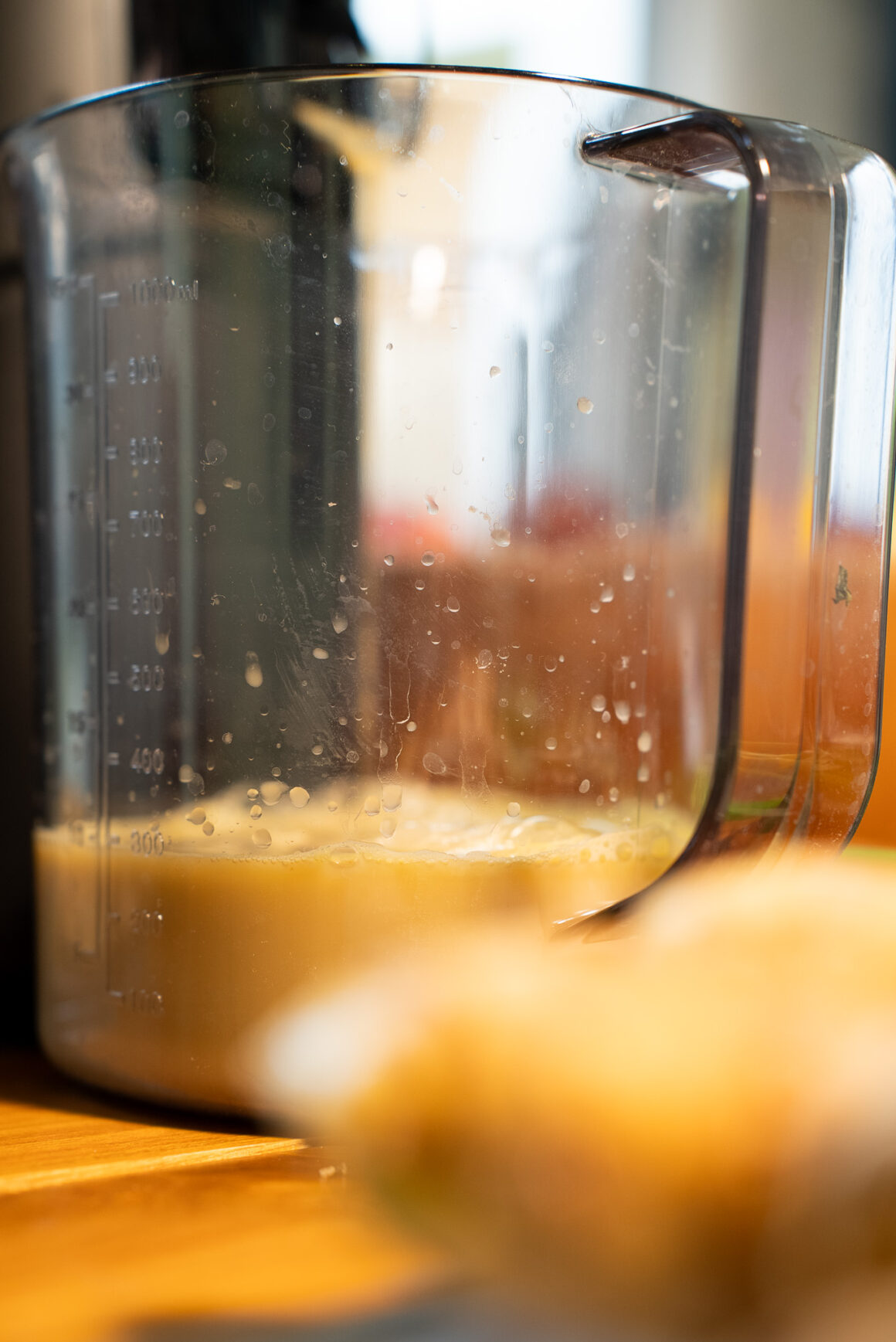 Messbecher mit frisch gepresstem Saft am Hurom H70-ST – Skala sichtbar, feiner Schaumrand, Küchenlicht.