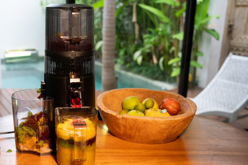 Hurom H70-ST auf Holztisch neben Obstschale – natürliche Küchenkulisse für veganes Cold-Press-Juicing.