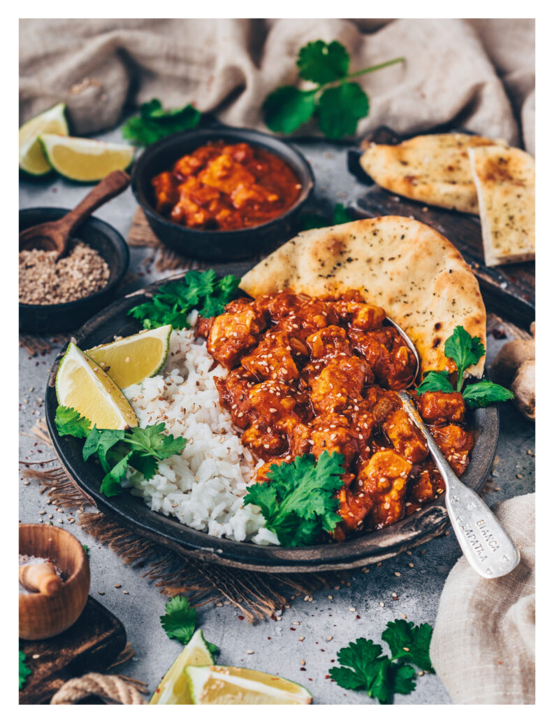 Cremiges veganes Butter Chicken mit Tofu, serviert mit Reis, Naan und frischen Kräutern