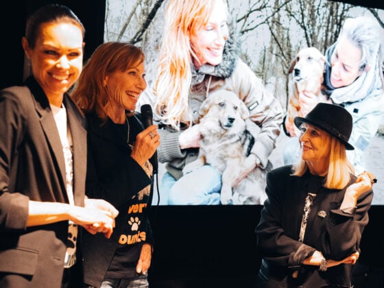 Sabine Peschke (links) spricht ins Mikrofon neben Schauspielerin Andrea Sawatzki (Mitte) und Journalistin Patricia Riekel beim Charity-Event von Giulia & Romeo in München. Im Hintergrund ein Bildschirm mit einem Straßenhund für das Projekt von NaTiNo e.V.