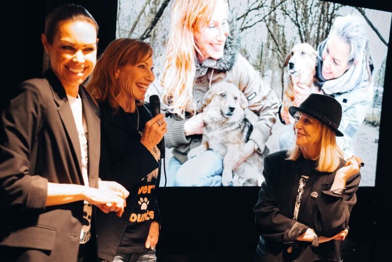 Sabine Peschke (links) spricht ins Mikrofon neben Schauspielerin Andrea Sawatzki (Mitte) und Journalistin Patricia Riekel beim Charity-Event von Giulia & Romeo in München. Im Hintergrund ein Bildschirm mit einem Straßenhund für das Projekt von NaTiNo e.V.