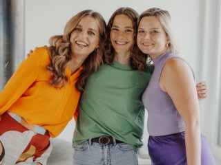 Fitgreenmind Gründerinnen Jennifer Reinhard, Maya Leinenbach und Kristina Kull stehen Arm in Arm in einem hellen StartUp-Büro