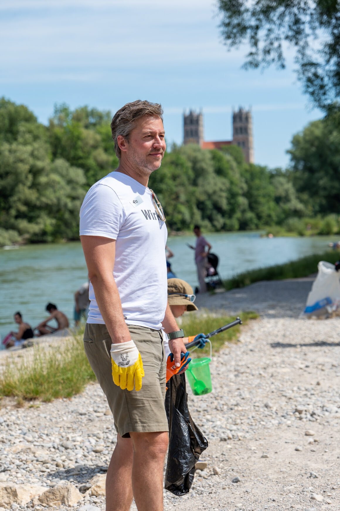 Florian Henle, Gründer von Polarstern, sammelt Müll beim Isar Clean-Up in München mit Arbeitshandschuhen und Müllsack, im Hintergrund die Frauenkirche