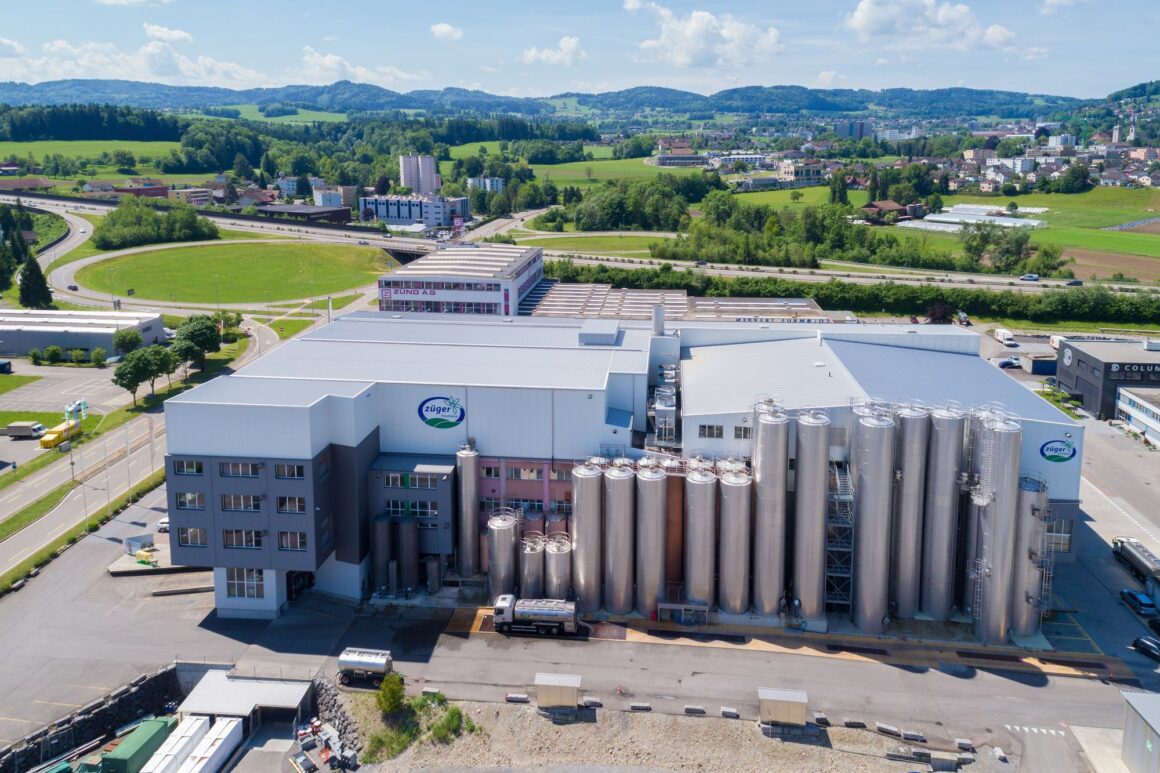 Luftaufnahme des Züger Frischkäse Produktionsstandorts in Oberbüren Schweiz mit modernen Produktionshallen, Silotanks und grüner Ostschweizer Landschaft im Hintergrund