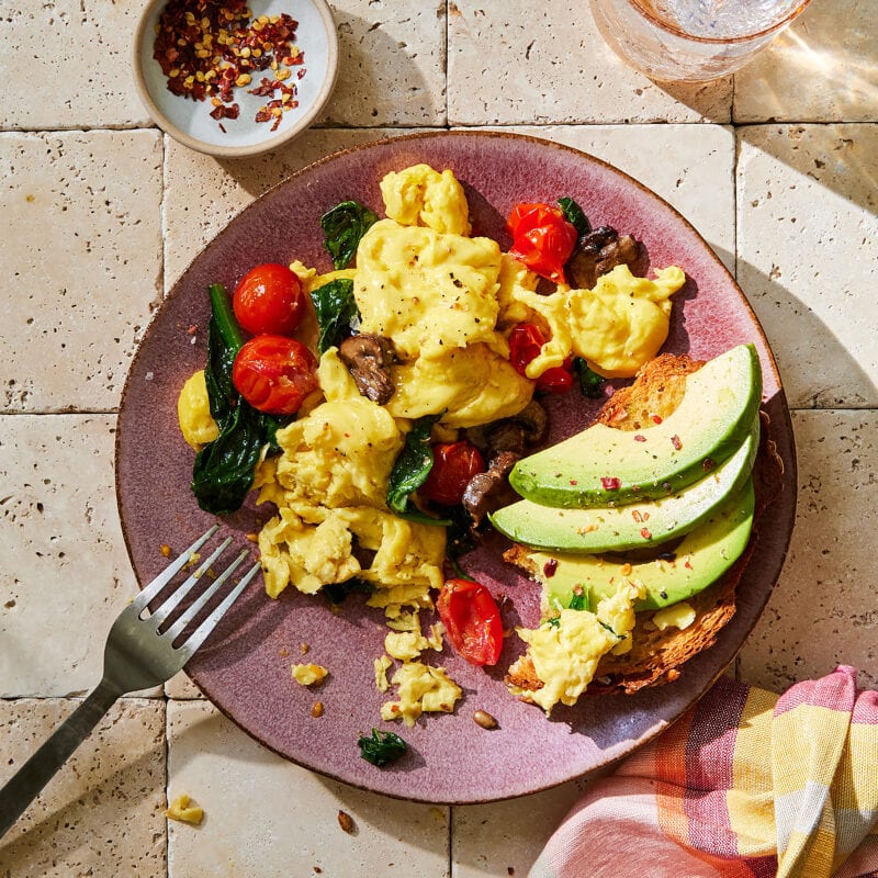 Veganes Rührei mit Avocado, Kirschtomaten und Spinat auf einem Teller.