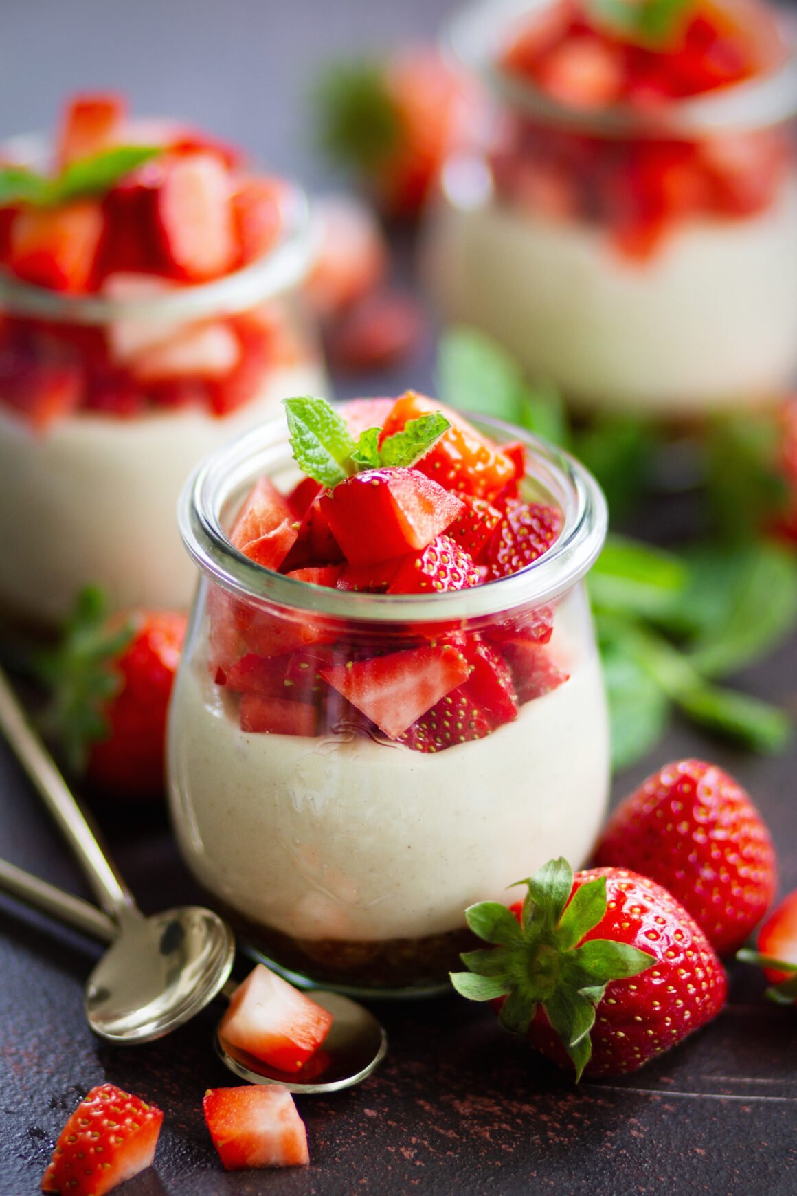 Veganer No Bake Erdbeer-Cheesecake im Glas mit cremiger Cashewfüllung, frischen Erdbeerwürfeln und Minze, angerichtet in Weckgläsern