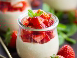 Veganer No Bake Erdbeer-Cheesecake im Glas mit cremiger Cashewfüllung, frischen Erdbeerwürfeln und Minze, angerichtet in Weckgläsern