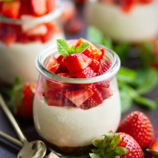 Veganer No Bake Erdbeer-Cheesecake im Glas mit cremiger Cashewfüllung, frischen Erdbeerwürfeln und Minze, angerichtet in Weckgläsern