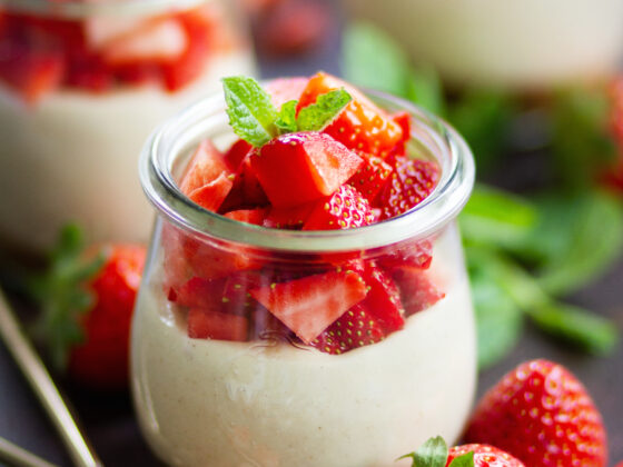Veganer No Bake Erdbeer-Cheesecake im Glas mit cremiger Cashewfüllung, frischen Erdbeerwürfeln und Minze, angerichtet in Weckgläsern