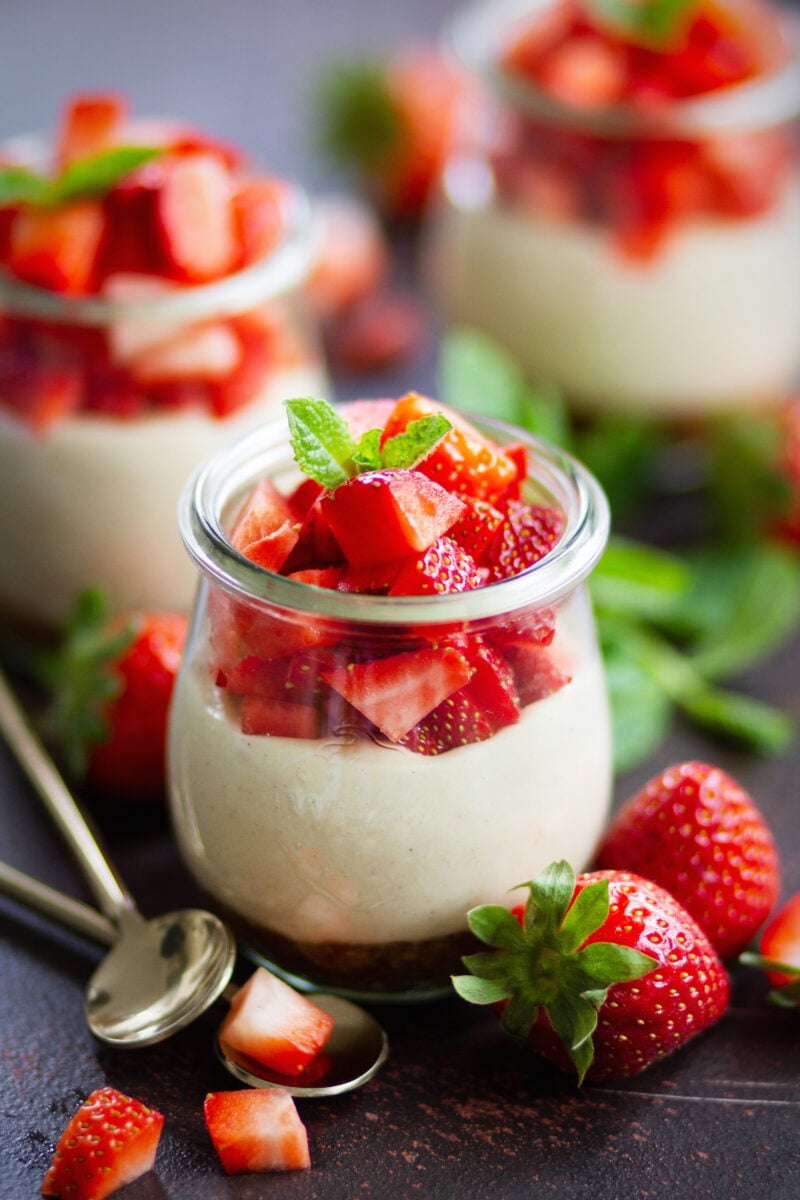 Veganer No Bake Erdbeer-Cheesecake im Glas mit cremiger Cashewfüllung, frischen Erdbeerwürfeln und Minze, angerichtet in Weckgläsern