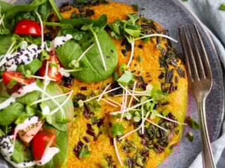 Veganes Kichererbsen-Omelette mit frischen Kräutern, Babyspinat, Cherrytomaten, Sprossen und Sojajoghurt auf grauem Keramikteller