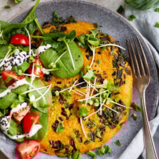 Veganes Kichererbsen-Omelette mit frischen Kräutern, Babyspinat, Cherrytomaten, Sprossen und Sojajoghurt auf grauem Keramikteller