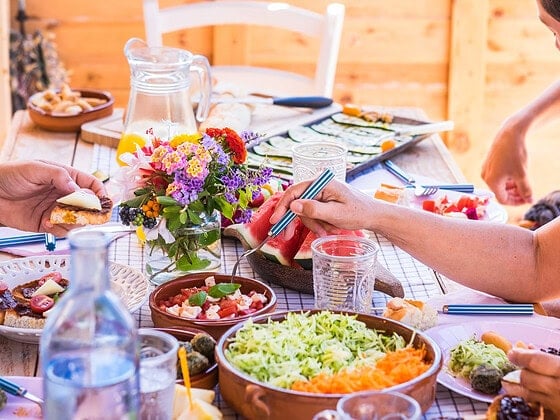 Gedeckter Holztisch im Freien mit veganem Brunch aus Salaten, Wassermelone, Brot und Blumen
