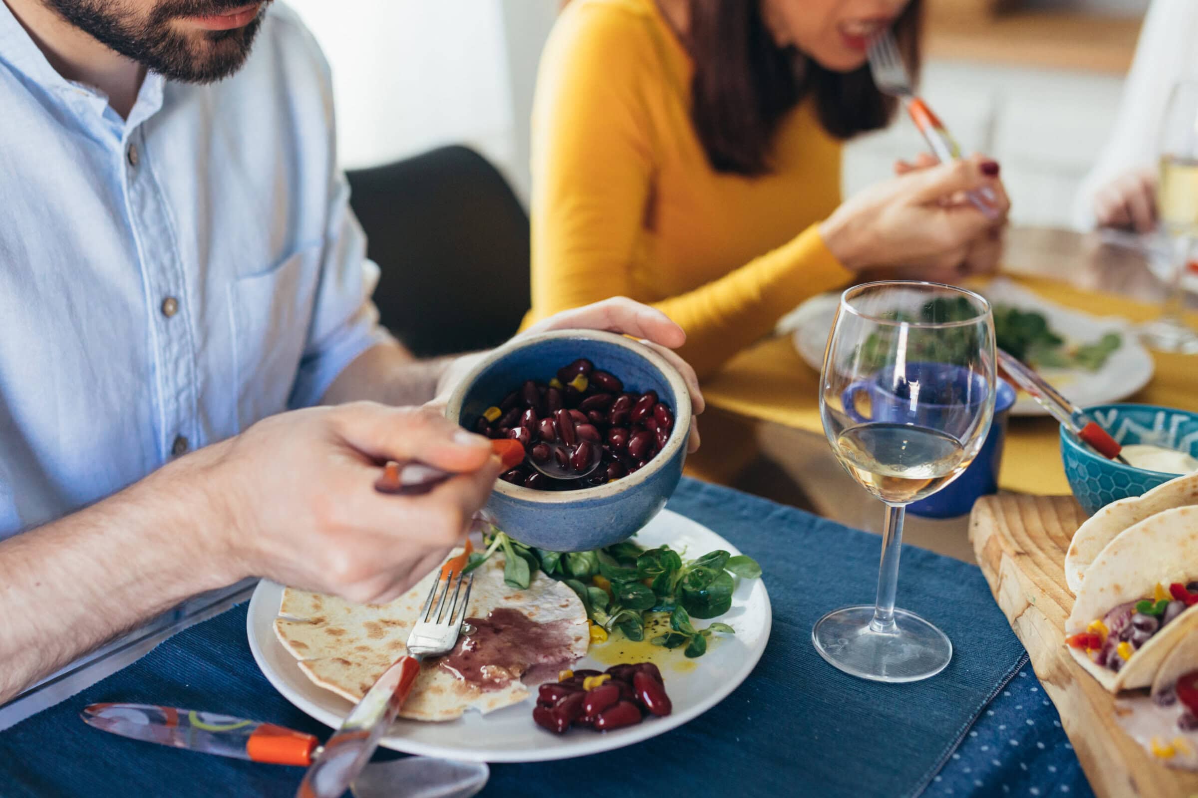 Junger Mann isst Kidney-Bohnen mit Tacos und Salat am gedeckten Esstisch
