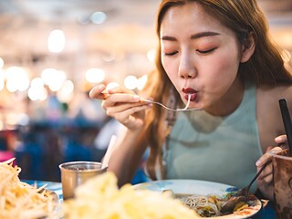 Person mit Rucksack vor exotischer Streetfood-Szene, vegan reisen in Asien mit Buddha Bowl in der Hand