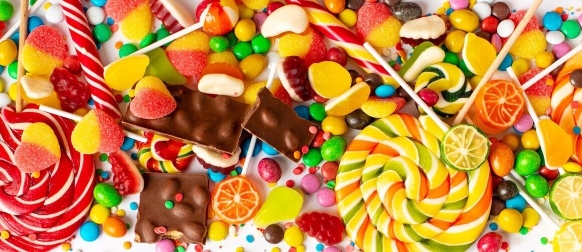 Vegane Süßigkeiten verschiedener Marken auf Holzbrett – Schokolade, Gummibärchen, Riegel und Bonbons
