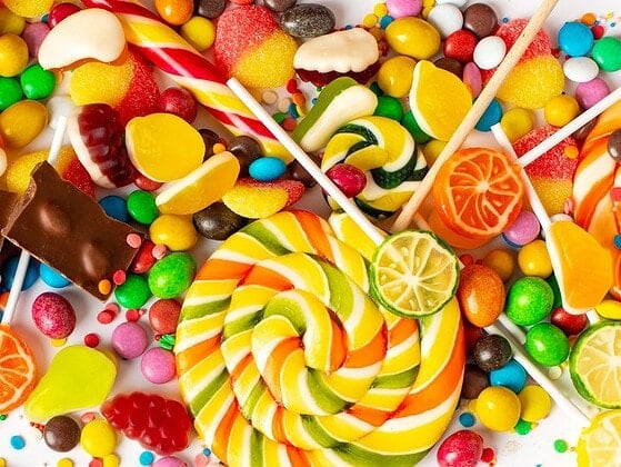 Vegane Süßigkeiten verschiedener Marken auf Holzbrett – Schokolade, Gummibärchen, Riegel und Bonbons