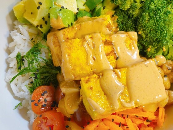 Vegane Buddha-Bowl mit gebratenem Tofu, Reis, Avocado, Brokkoli, Karotten und Kirschtomaten
