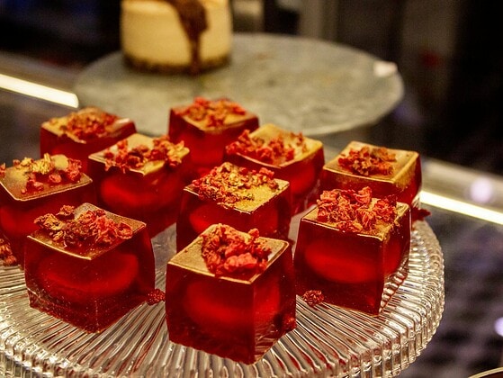 Rote Götterspeise-Würfel mit getrockneten Himbeeren auf einer Glasetagere in einer Vitrine