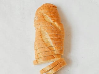 Frisch gebackenes Brot in Scheiben geschnitten auf Holzbrett, dahinter Kornkranz