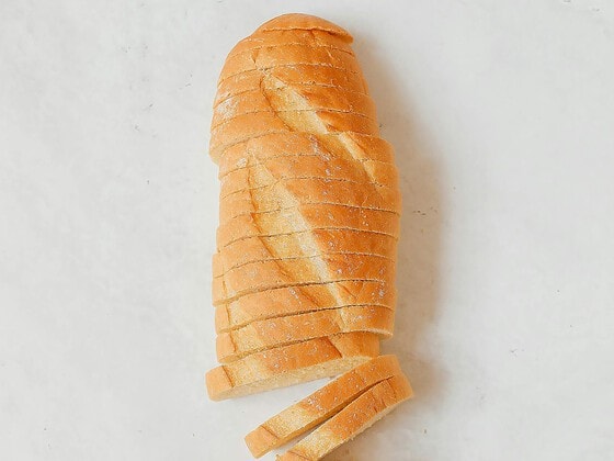 Frisch gebackenes Brot in Scheiben geschnitten auf Holzbrett, dahinter Kornkranz