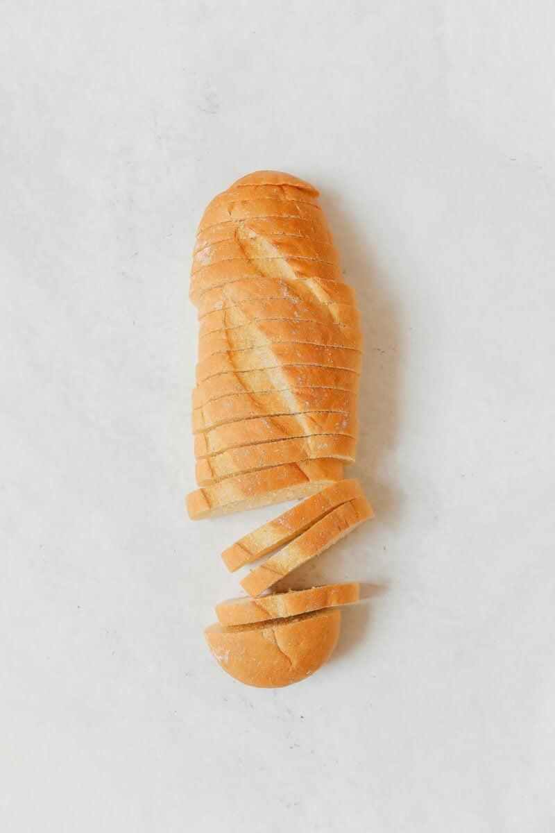 Frisch gebackenes Brot in Scheiben geschnitten auf Holzbrett, dahinter Kornkranz