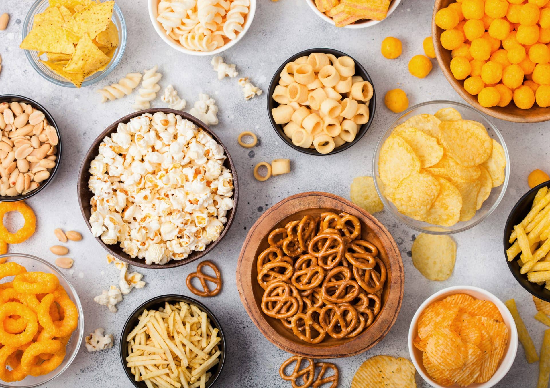 Verschiedene Knabber-Snacks in Schüsseln: Chips, Popcorn, Brezeln und Erdnüsse