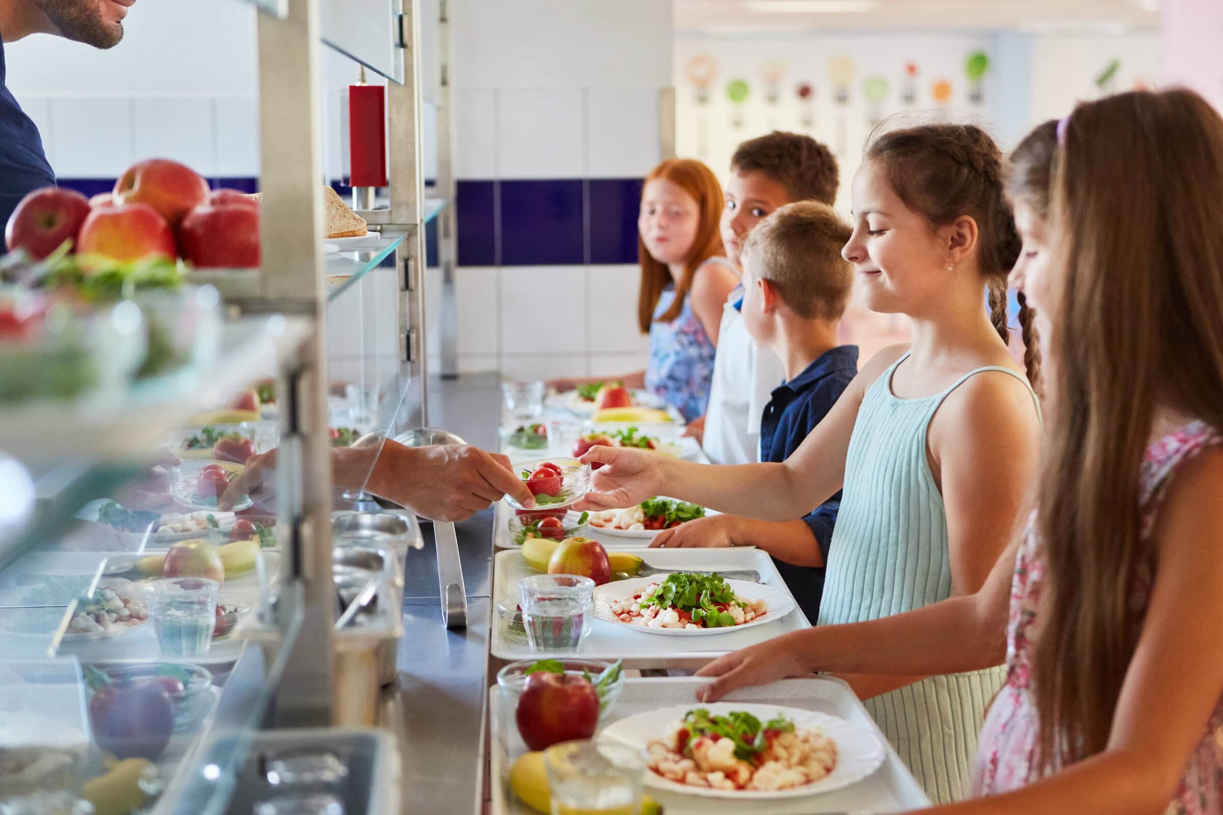 Schulkinder warten an der Essensausgabe einer Schulkantine mit gesunden Mittagessen-Tabletts