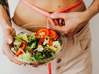 Frische Gemüseplatte mit Hülsenfrüchten, Quinoa und einer Personenwaage, helle Küche im Hintergrund