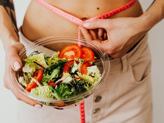 Frische Gemüseplatte mit Hülsenfrüchten, Quinoa und einer Personenwaage, helle Küche im Hintergrund