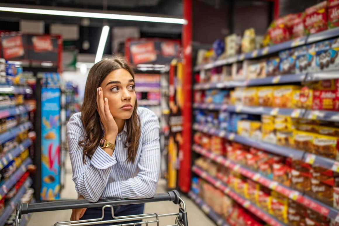 Frau steht unschlüssig vor dem Süßigkeitenregal im Supermarkt