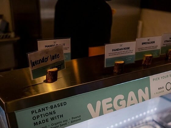 Verschiedene vegane Eissorten in Schalen und am Stiel, sommerlich auf Holztisch mit Beeren und Minze