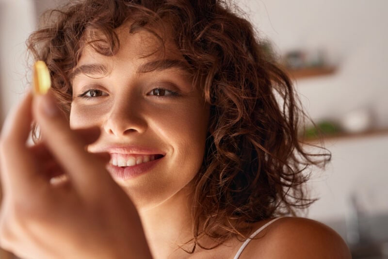 Junge Frau mit Locken hält vegane Omega-3-Kapsel