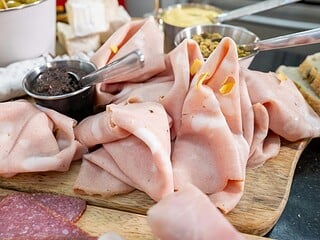 Veganer Aufschnitt in verschiedenen Sorten auf Holzbrett, daneben Brötchen, Senf und Gurke