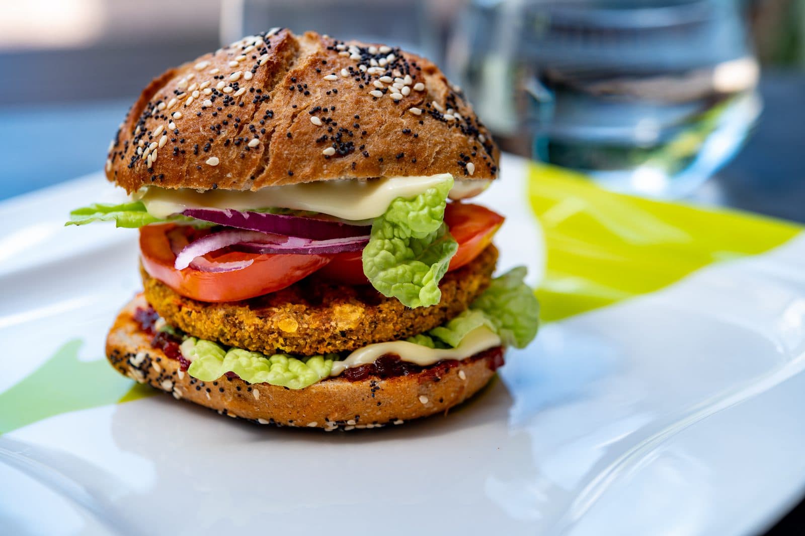 Aufgeschnittener veganer Burger im Bun mit Patty, Salat, Tomate und Sauce